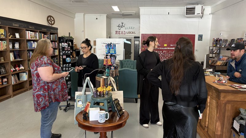 People browsing and chatting inside a local bookstore, with bookshelves, a reading nook, and gift displays.