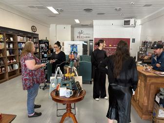 People browsing and chatting inside a local bookstore, with bookshelves, a reading nook, and gift displays.