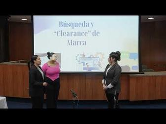 Video still of three presenters standing at a podium in front of a screen reading "Búsqueda y 'Clearance' de Marca."